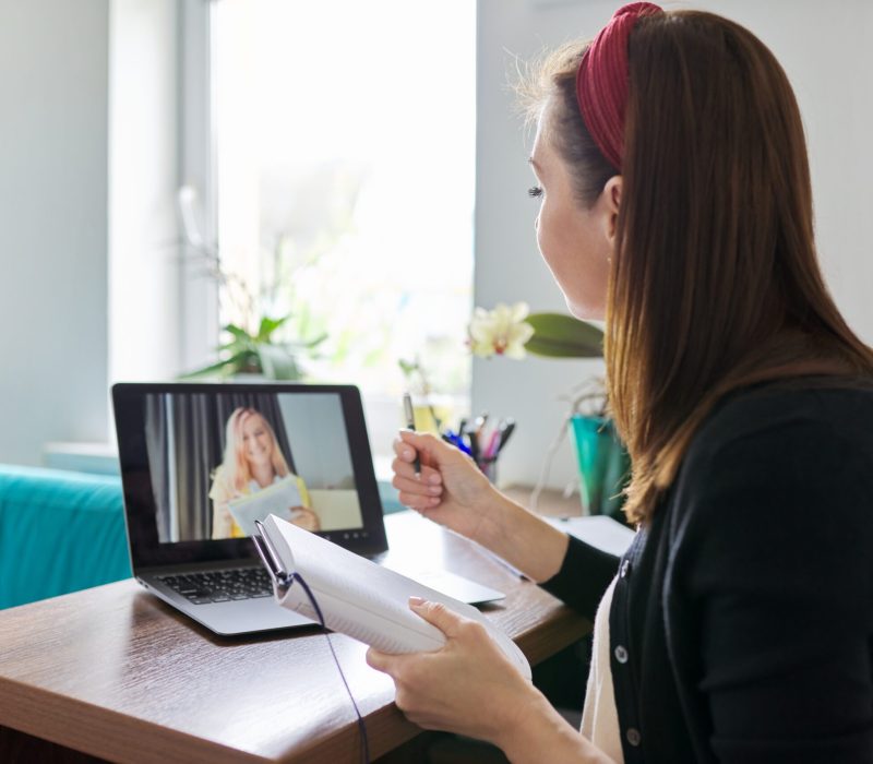 Woman teacher teaching at home online, distance learning. Female sitting at home at table with laptop on virtual meeting with teenage student, video call. E-learning modern technologies in education