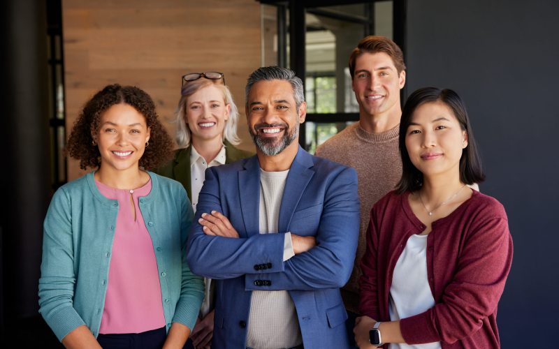 Group of diverse professionals posing in an office environment while smiling and looking at camera. Successful business group posing together at modern office. Middle eastern leadership with his multiethnic team expressing unity and confidence.